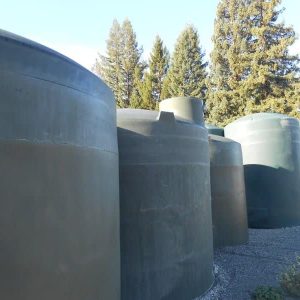 The image displays vertical polyethylene water storage tanks of various sizes.