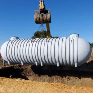 The image shows a large cylindrical cistern tank being installed.
